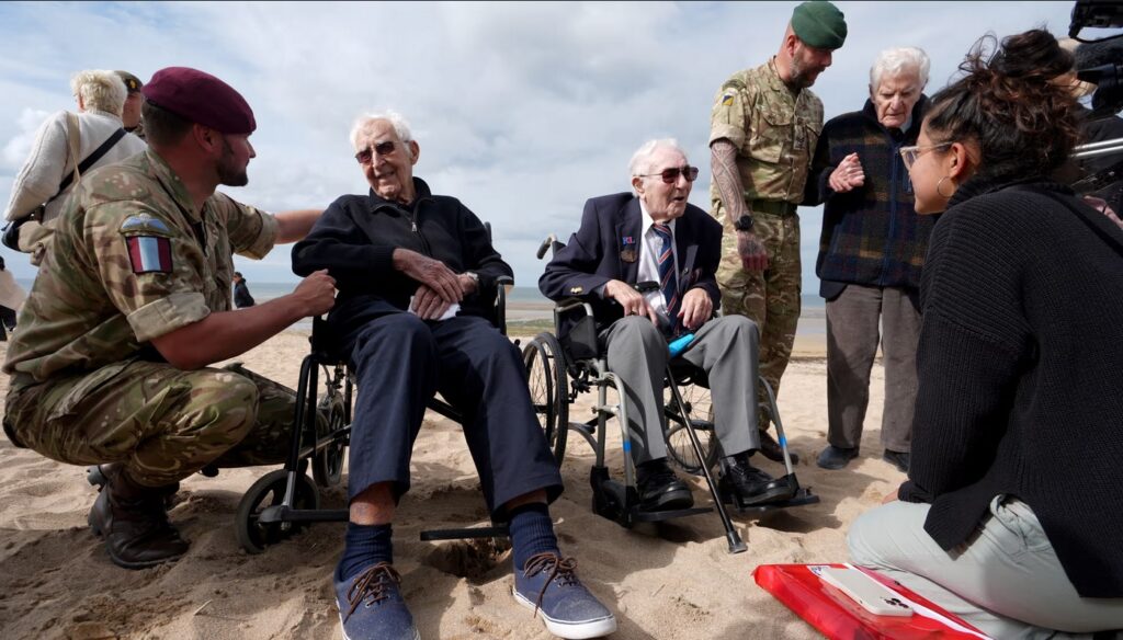 (De la stânga la dreapta) Cpl Aaron Stone cu veteranii John Life și Donald Jones se întorc pe plaja Sword din Normandia, Franța, unde au aterizat în ziua Z